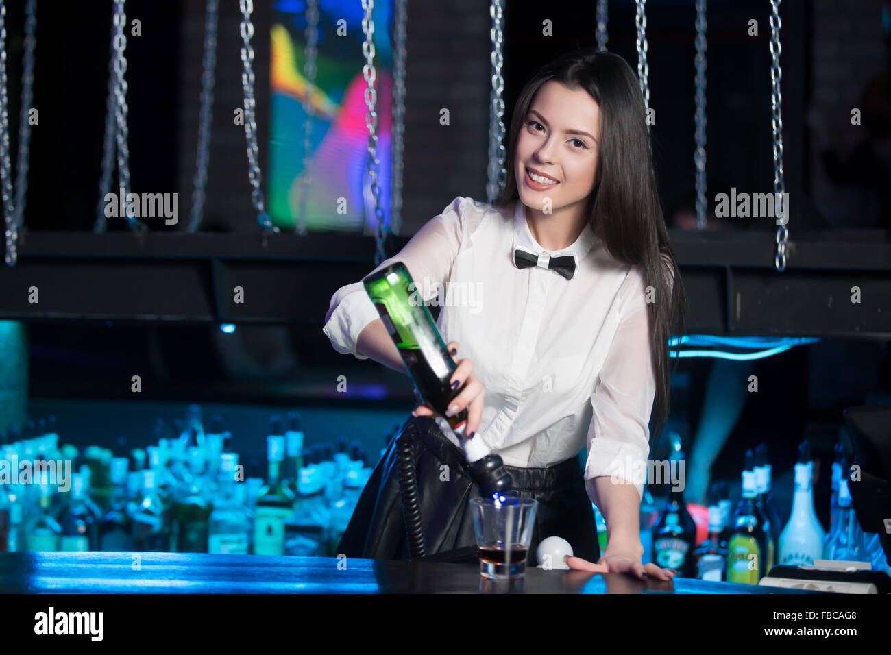 Schöne fröhliche Brünette Barkeeper Mädchen in weißem Hemd und schwarzer Fliege dienen Alkohol Getränk an der Theke, hält bottl Stockfoto
