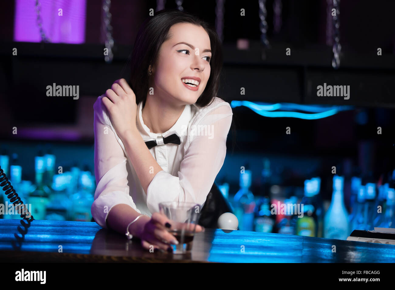 Schön fröhlich lächelnd Brünette Mädchen in weißem Hemd und schwarzer Fliege im Nachtclub bar, Glas mit Getränk Stockfoto