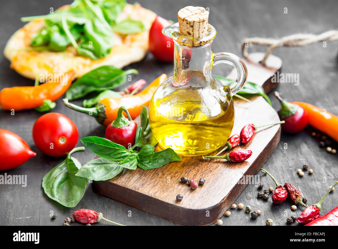 Olivenöl mit Gewürzen und Kräutern auf Holzbrett mit Tomaten und Paprika Stockfoto