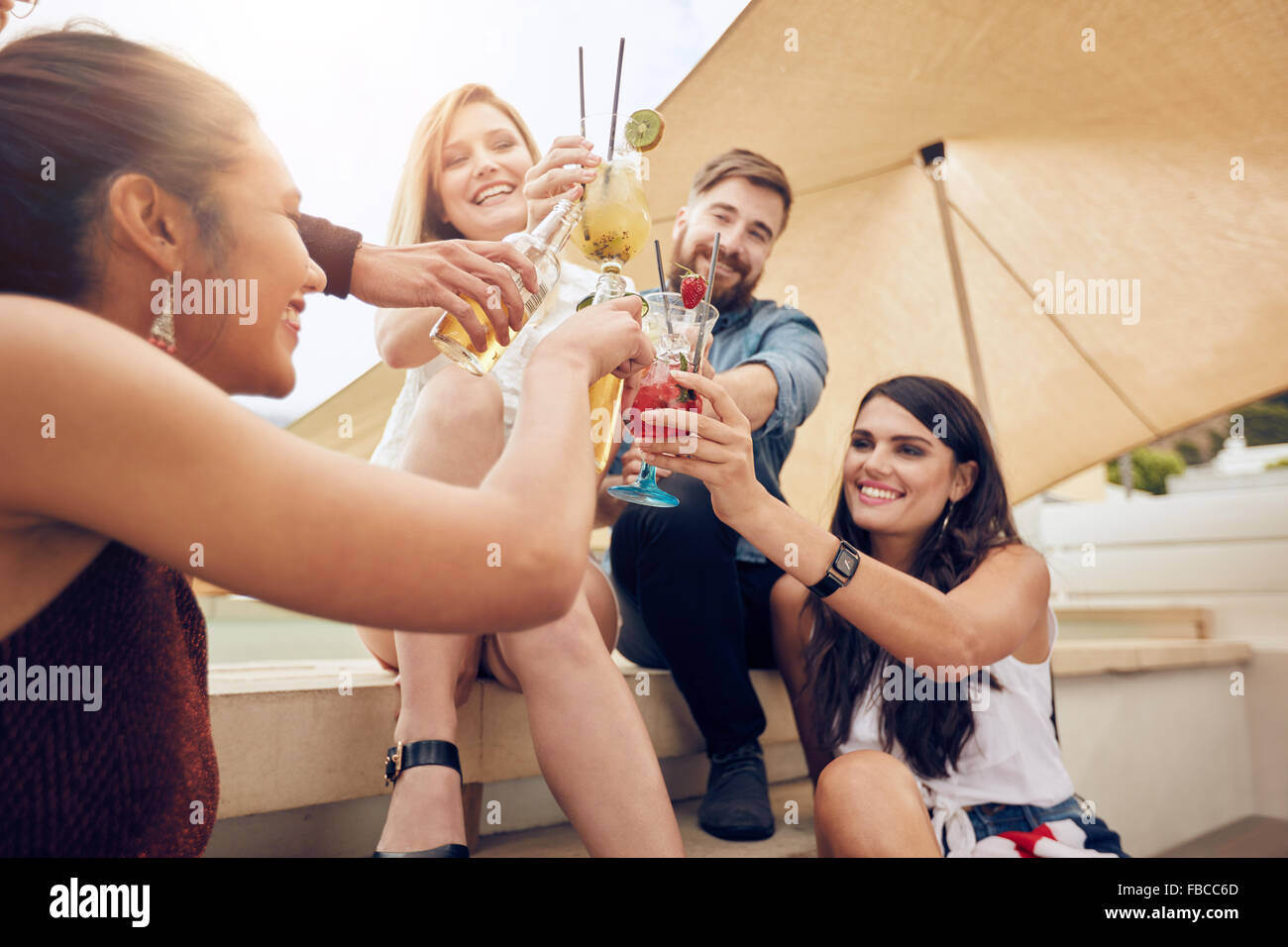 Gruppe von glücklichen Jugendlichen Jubel mit Cocktails und Lächeln während Sie feiern zusammen auf Dach. Gemischtrassig jungen Freunde ha Stockfoto