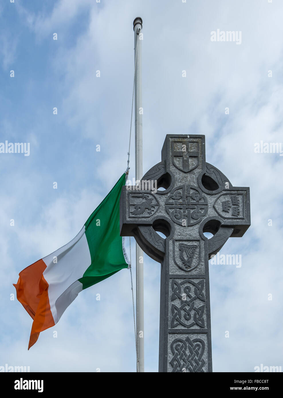 Eine irische Trikolore fliegt auf einem Mast hinter eine traditionelle irische keltische Kreuz auf Halbmast. Stockfoto