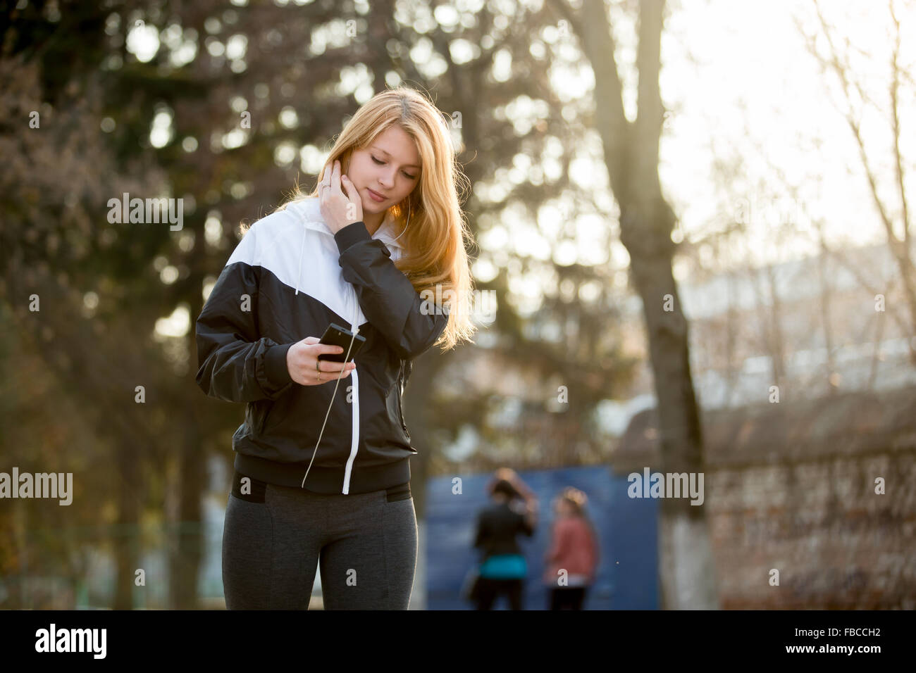 Jogger-Mädchen mit Kopfhörern in Sportbekleidung mit ihrem Smartphone vor morgen joggen Praxis auf der Straße Stockfoto