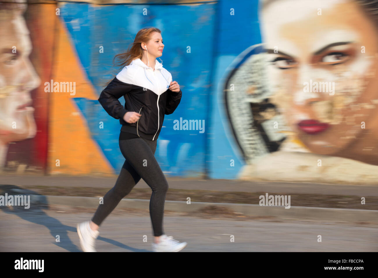 Schöne sportliche Mädchen tragen Läufer Sportbekleidung im Ohrhörer in der Stadt von morgen durch helle Graffitiwand, gesunde Activ laufen Stockfoto
