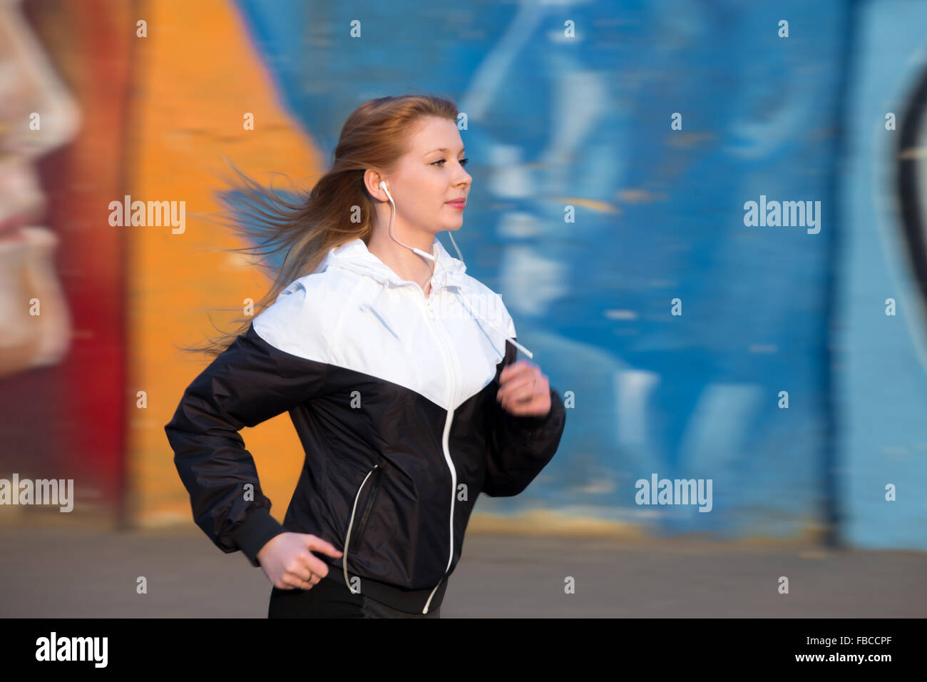 Schöne sportliche Läufer Mädchen Sportswear mit Geschwindigkeit in der Stadt von Morgen neben hellen Graffitiwand, Musik hören Stockfoto