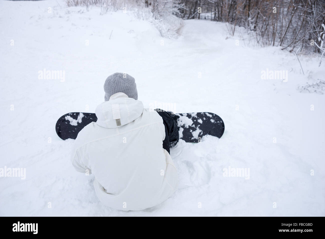 Junger Mann seinem Snowboard im Schnee einstellen, wie er sitzt mit dem Rücken zur Kamera, die Vorbereitung einer Abfahrt auf der Piste Stockfoto