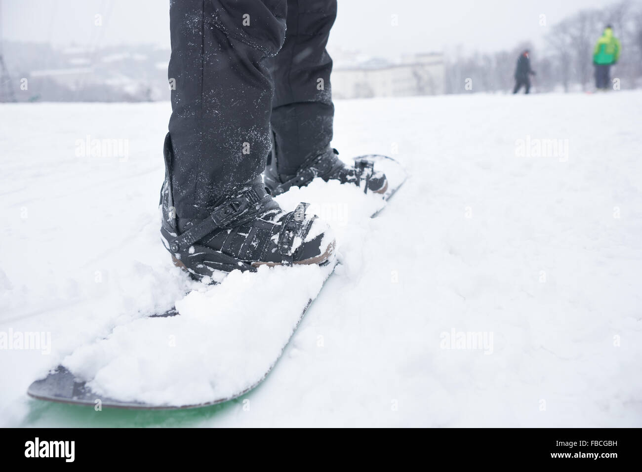 Beine und Verwaltungsrat ein Snowboarder auf einem verschneiten Berg, niedrigen Winkel mit Skifahrer, die in der Ferne sichtbar Stockfoto