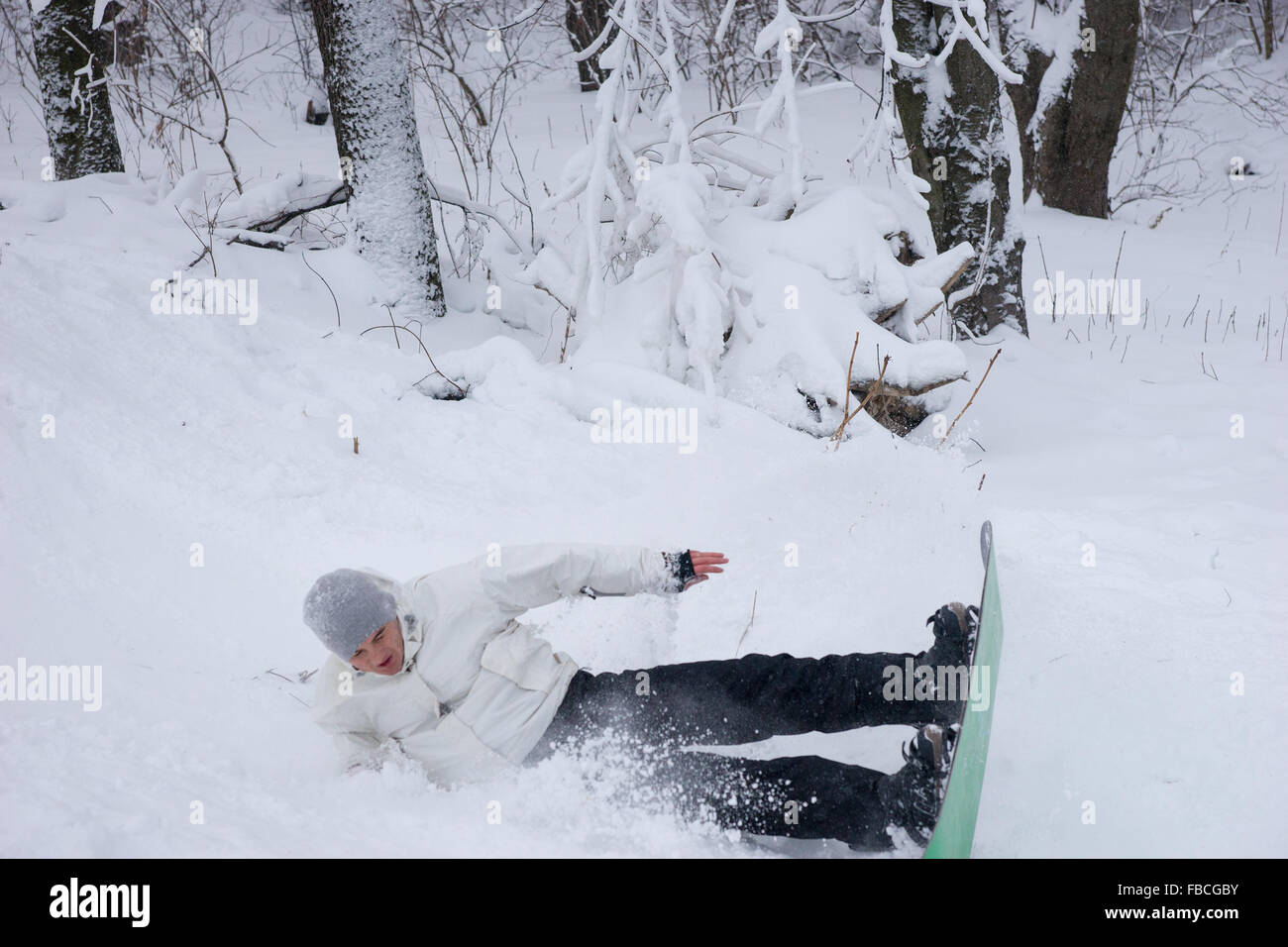 Junger Mann üben einen Sprung auf seinem Snowboard Landung auf seiner Seite im Schnee in einer Flut von Schneeflocken Stockfoto