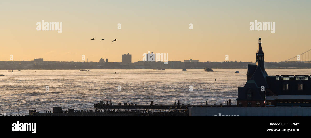 Drei Gänse fliegen über den Hudson-River in Richtung NYC an einem kalten Wintermorgen, wie die warme Sonne den Fluss Dampf macht. Stockfoto