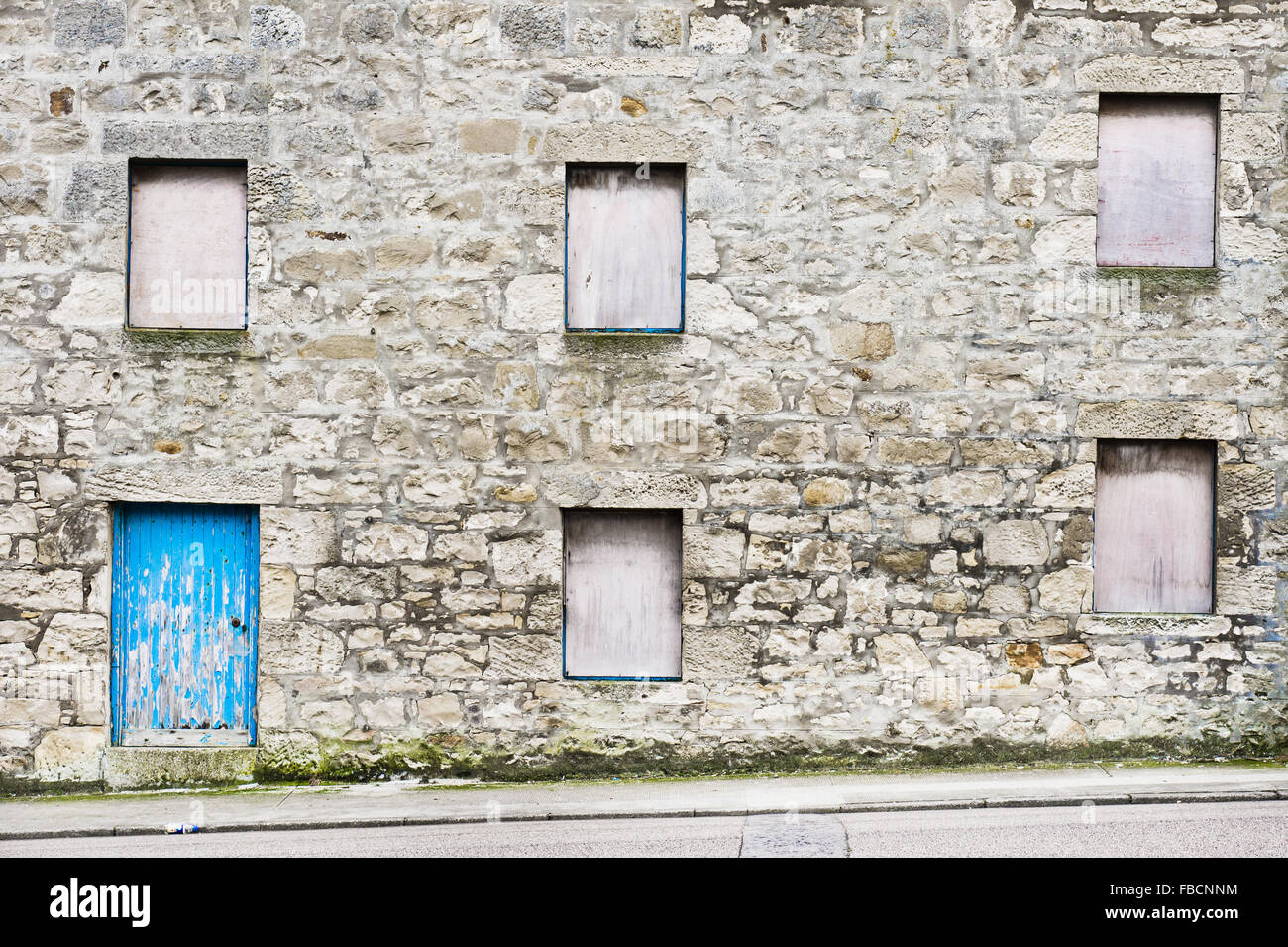 Teil der Fassade ein altes Steinhaus in Schottland mit Brettern vernagelt Windows eine blaue Holztür Stockfoto