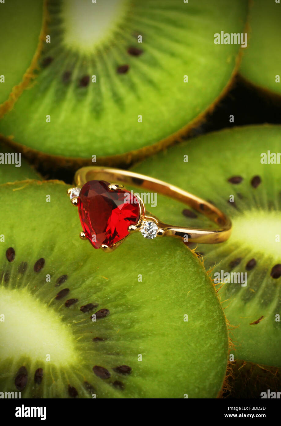 Goldener Ring mit roten Edelstein auf Kiwi Frucht Hintergrund, vertikale Zusammensetzung Stockfoto