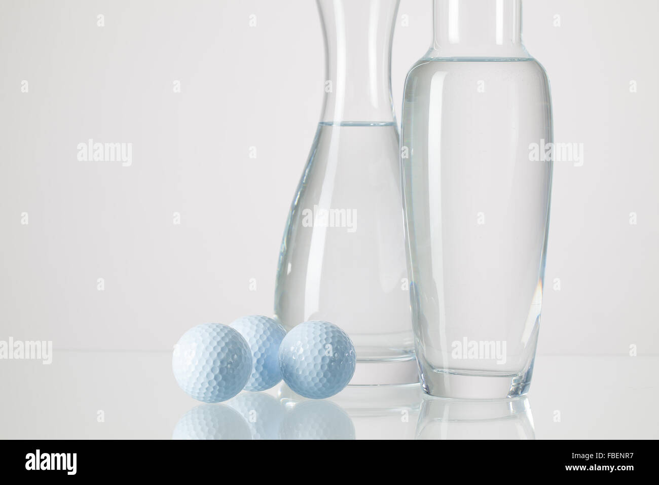 Zwei Vasen mit sauberem Wasser und Golfbälle auf einem Glastisch Stockfoto