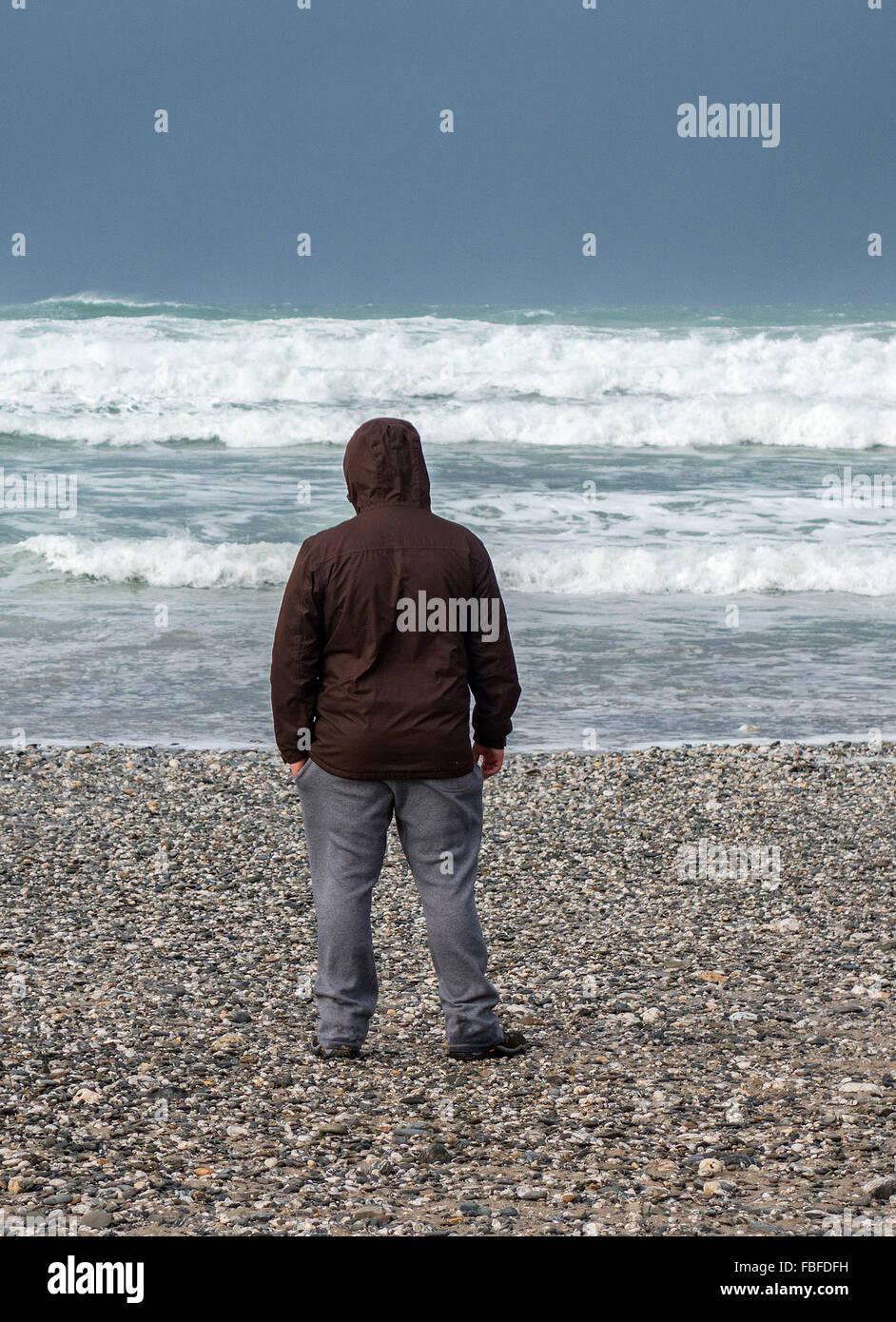 Mann auf einem Kiesstrand an der Küste mit Blick auf das Meer Stockfoto