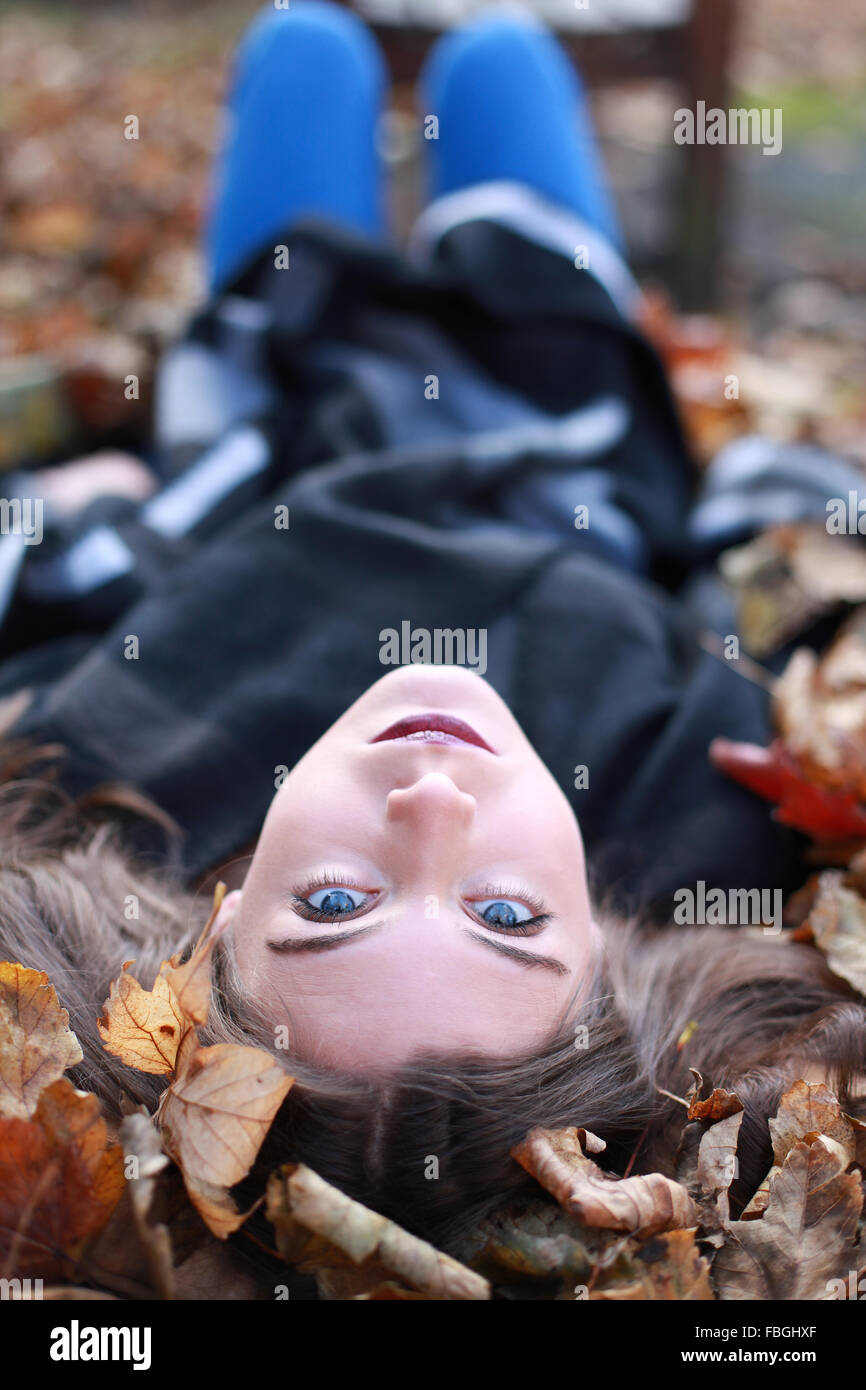 Junge Teenager-Mädchen kopfüber liegend auf einem Bett aus Blättern im Herbst Stockfoto