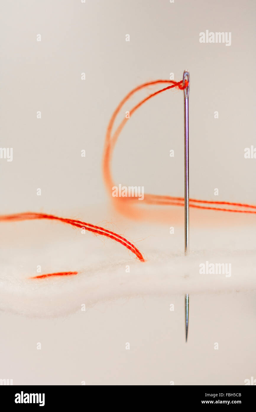 Eine Nadel, zwei Stücke aus weißem Stoff mit einem roten Faden zusammennähen. Stockfoto