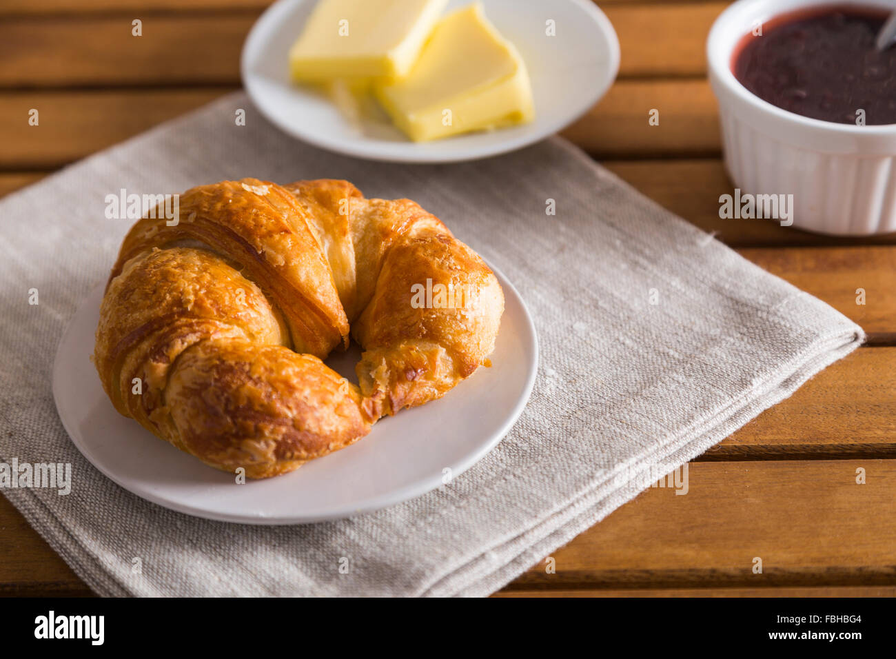 Französische Croissant Frühstück mit Scheiben Butter, einen Topf mit Erdbeermarmelade und eine graue Serviette Stockfoto