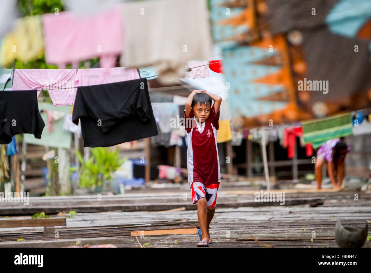 Ein Kind, das auf der Terrasse des Langhauses der traditionellen Dayak IBAN-Gemeinde in Sungai Utik, Kapuas Hulu, West Kalimantan, unter Wäscheleinen läuft. Stockfoto