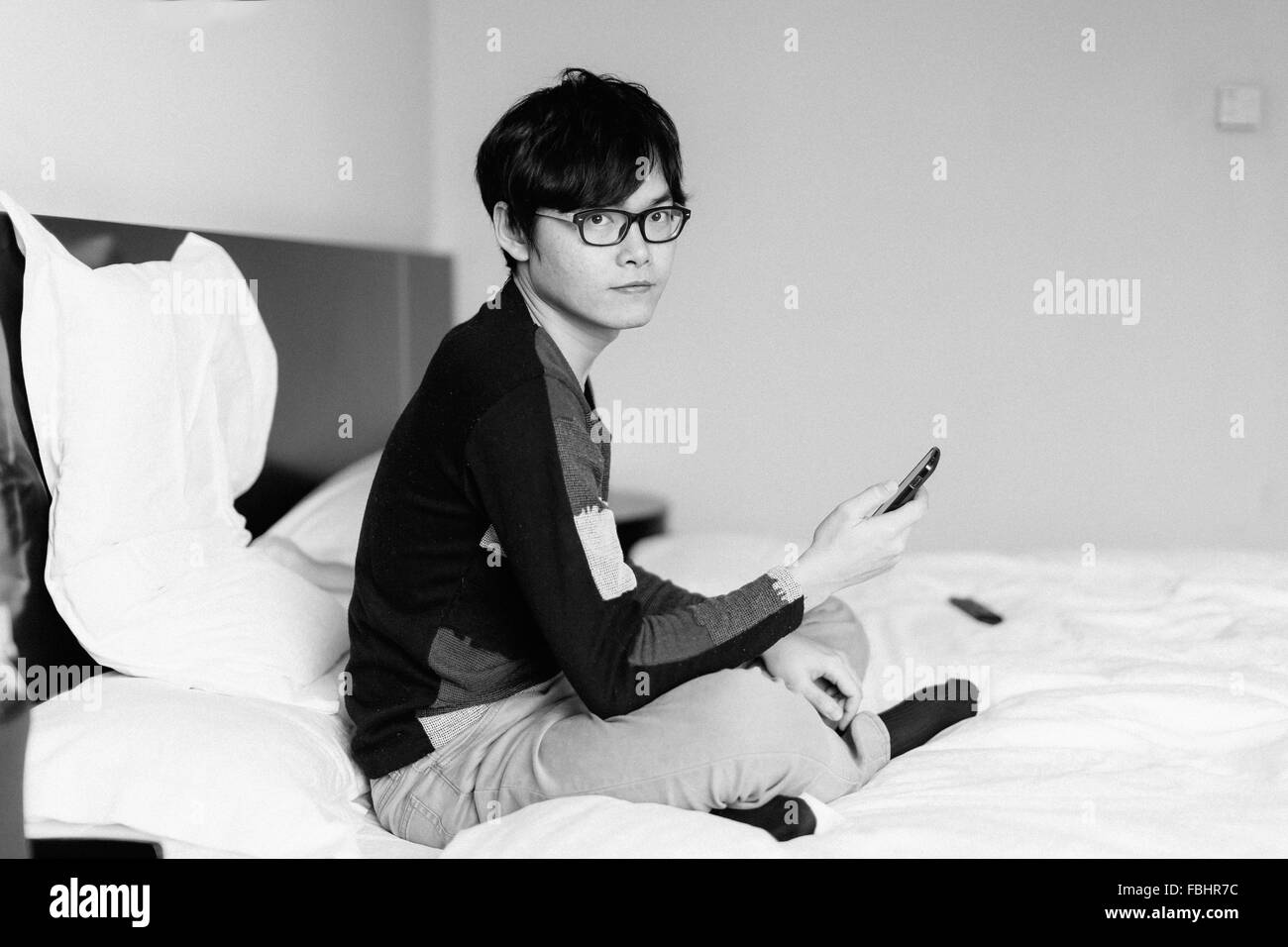 Asiatischer Mann spielen Telefon am Bett Stockfoto