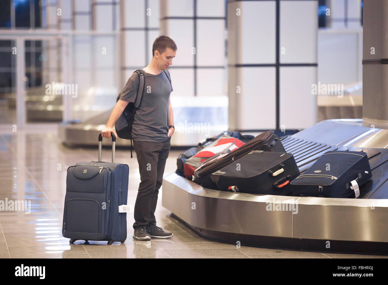 Schönen jungen Mann Passagier in seinen 20ern warten darauf, wählen Sie Gepäck am Gepäck-Förderbänder in der Ankunftshalle von terminal Flughafen bauen Stockfoto