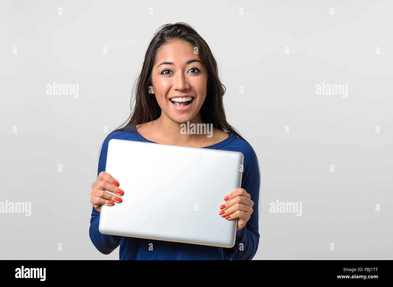 Begeistert junge Frau hält einen silbernen Laptop peering über der Oberseite mit einem strahlenden Lächeln der Vorfreude und Glee, Oberkörper auf wh Stockfoto