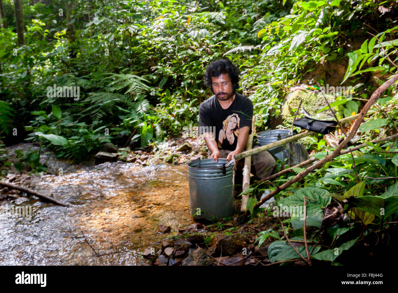 Ein Bauer, der Wasser an einem Bach in einem Wald am westlichen Rand des Ökosystems von Batang Toru in Central Tapanuli, Nordsumatra, Indonesien, nimmt. Stockfoto