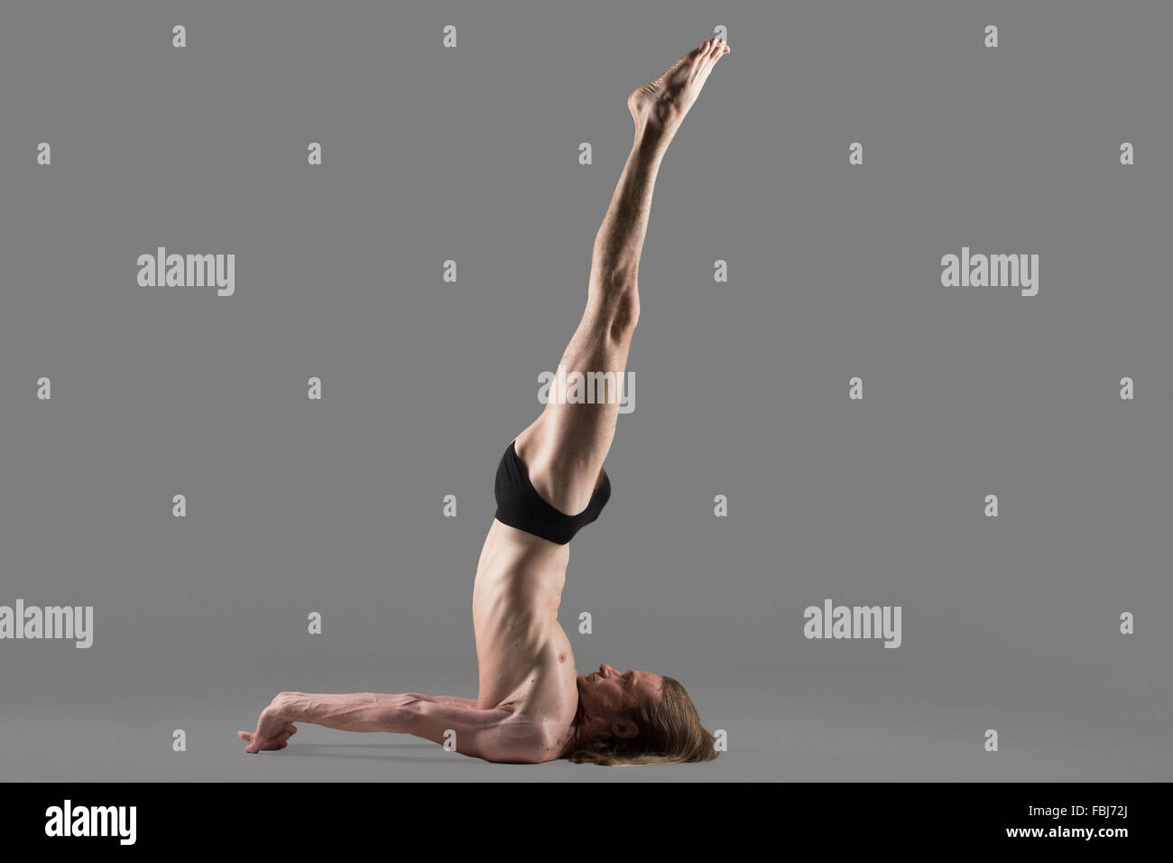 Sportlich muskulösen jungen Yogi Mann tut nicht unterstützte Shoulderstand Pose, Niralamba Sarvangasana, Studio gedreht auf dunklen grauen Hintergrund Stockfoto