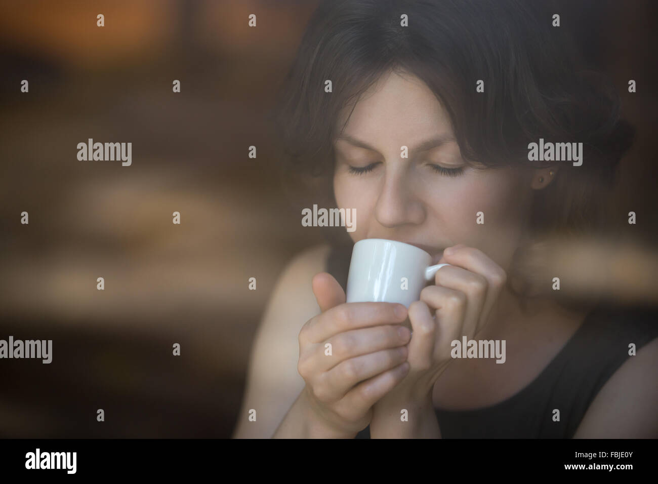 Porträt der schönen glücklich lächelnde junge Frau sitzt im modernen Café halten Kaffee, genießen Sie ihr Getränk mit Augen geschlossen Stockfoto