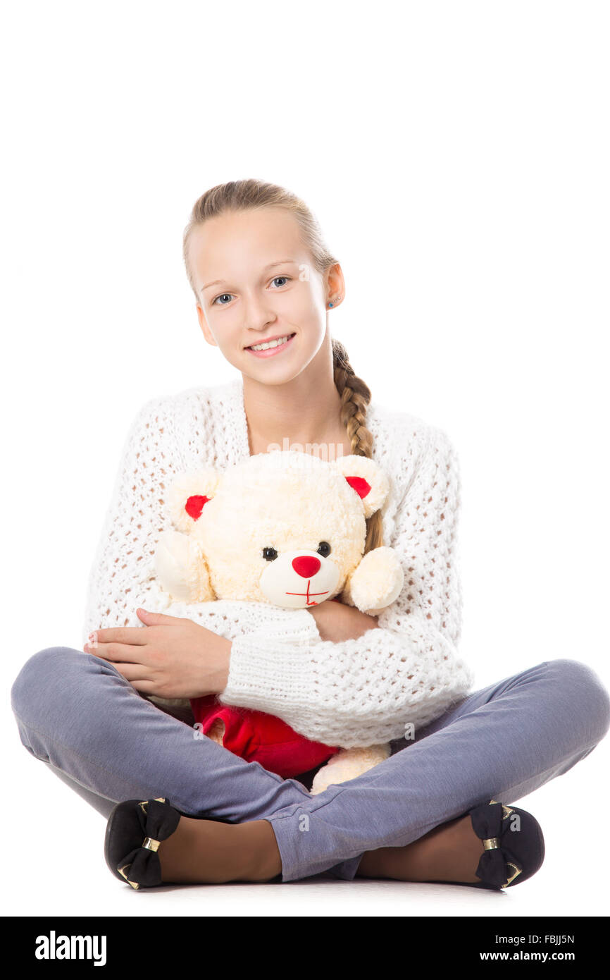 Porträt von glücklich schön lässig Teenager-Mädchen sitzt mit gekreuzten Beinen in Strickpullover umarmt Teddybär, freundlich lächelnd Stockfoto