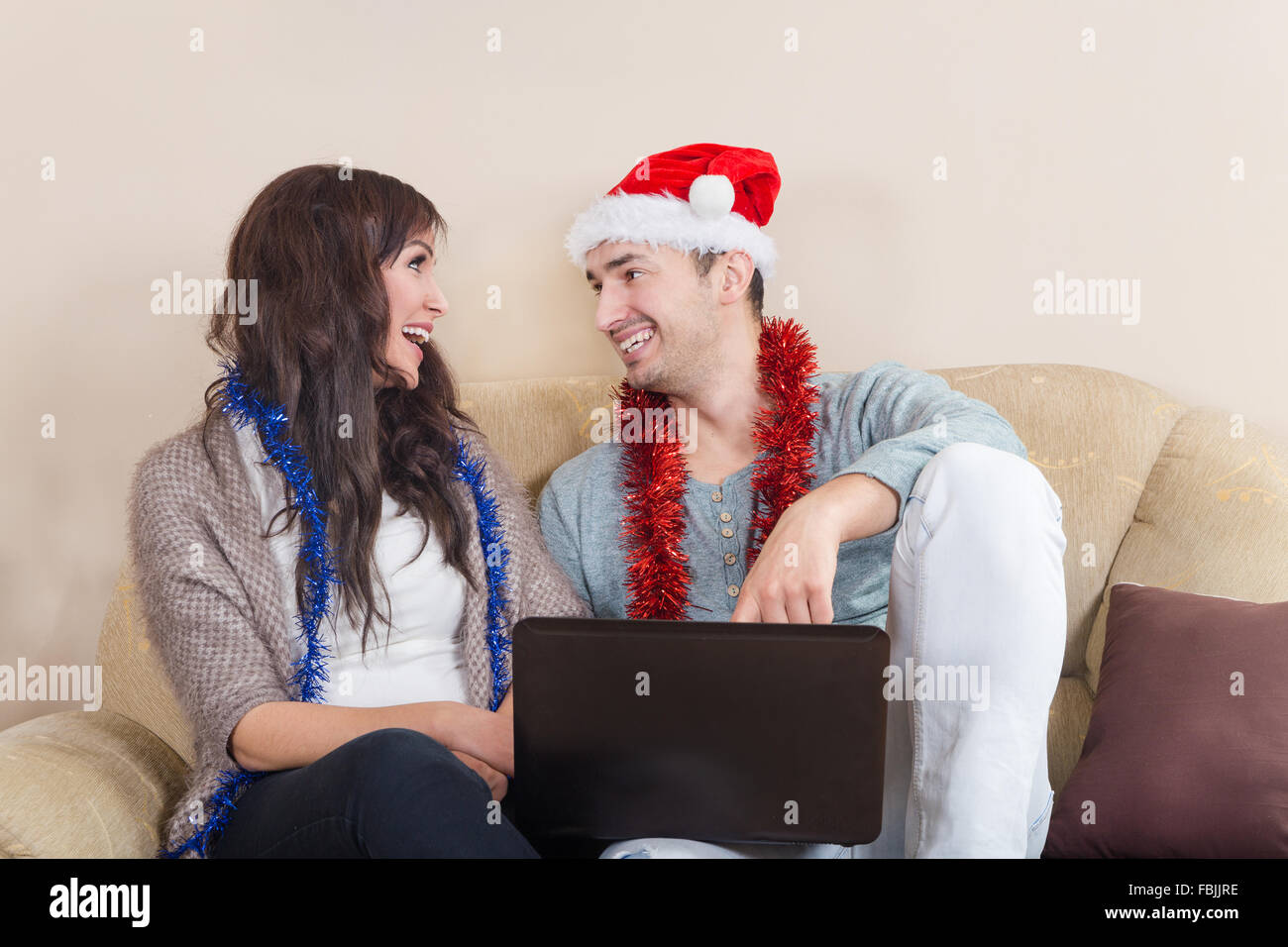 Glückliches Paar suchen Winterurlaub Destinationen auf Laptop, Weihnachtszeit. Junges attraktives Paar mit Weihnachtsmütze zusammen in Stockfoto