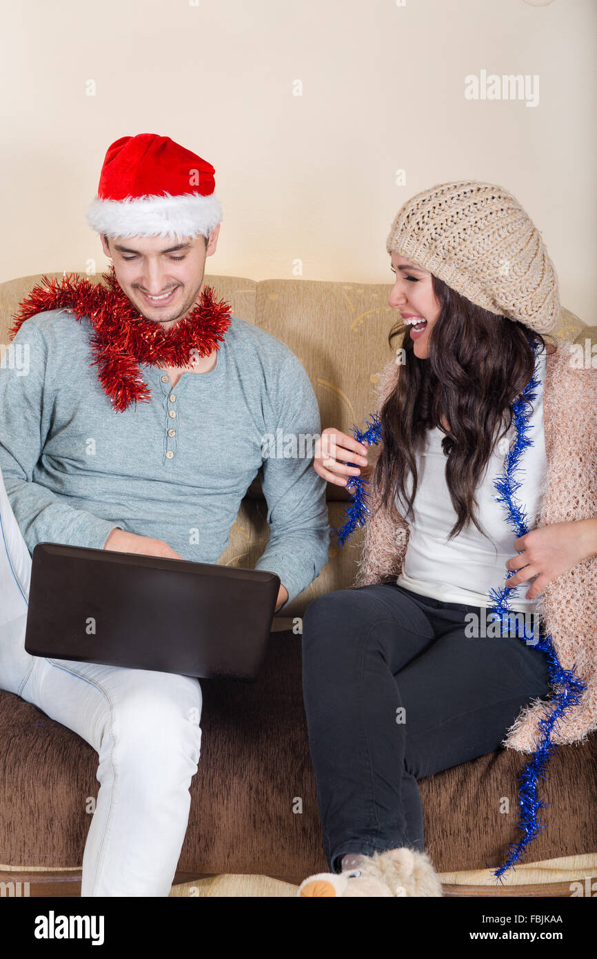 Glückliches Paar suchen Winterurlaub Destinationen auf Laptop, Weihnachtszeit. Junges attraktives Paar mit Weihnachtsmütze zusammen in Stockfoto