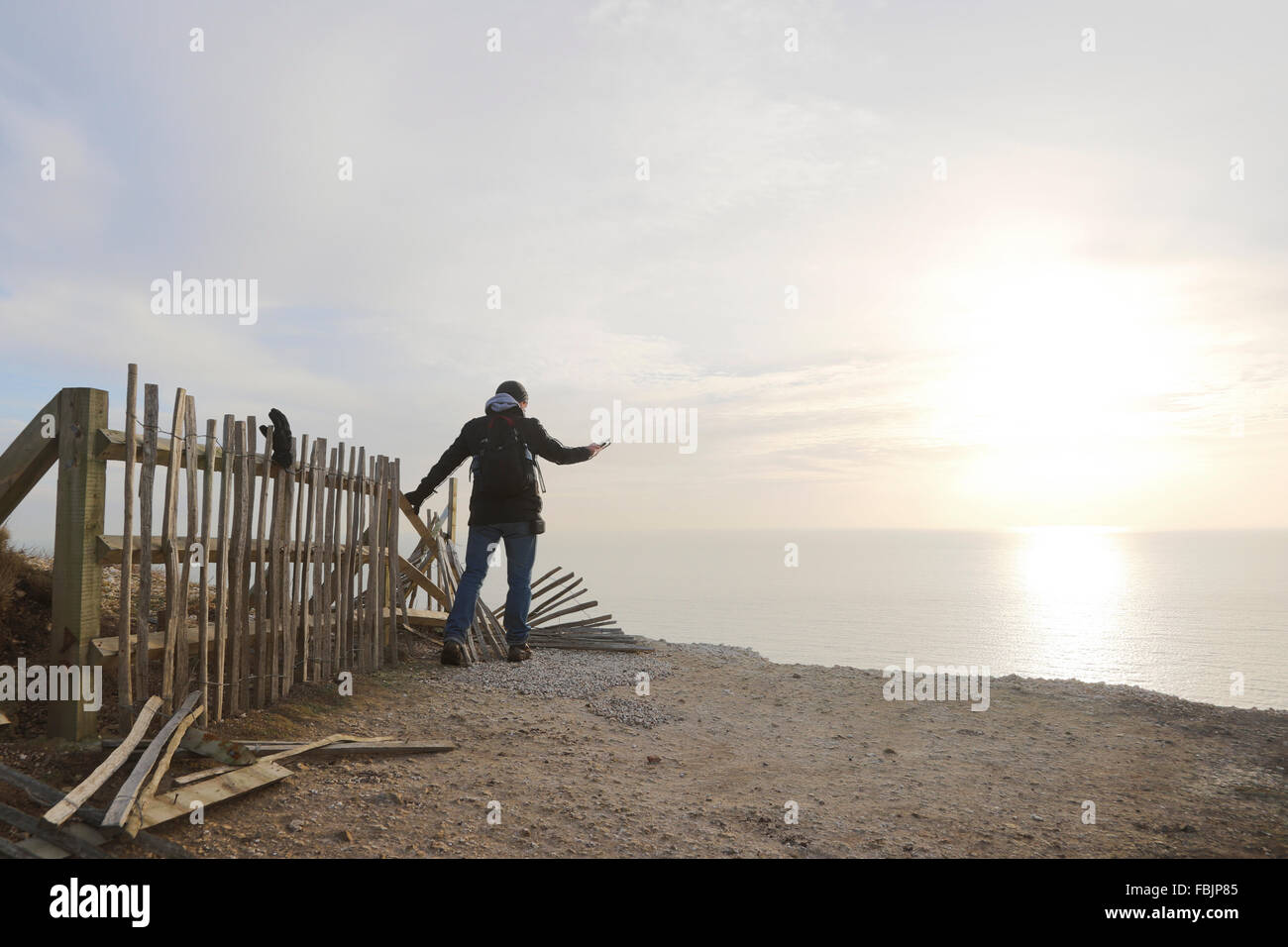 Ein Mann hält auf einen defekten Zaun, während ein Bild über den Rand die Klippe am Beachy Head mit Meer und Sonne in der Ferne. Stockfoto
