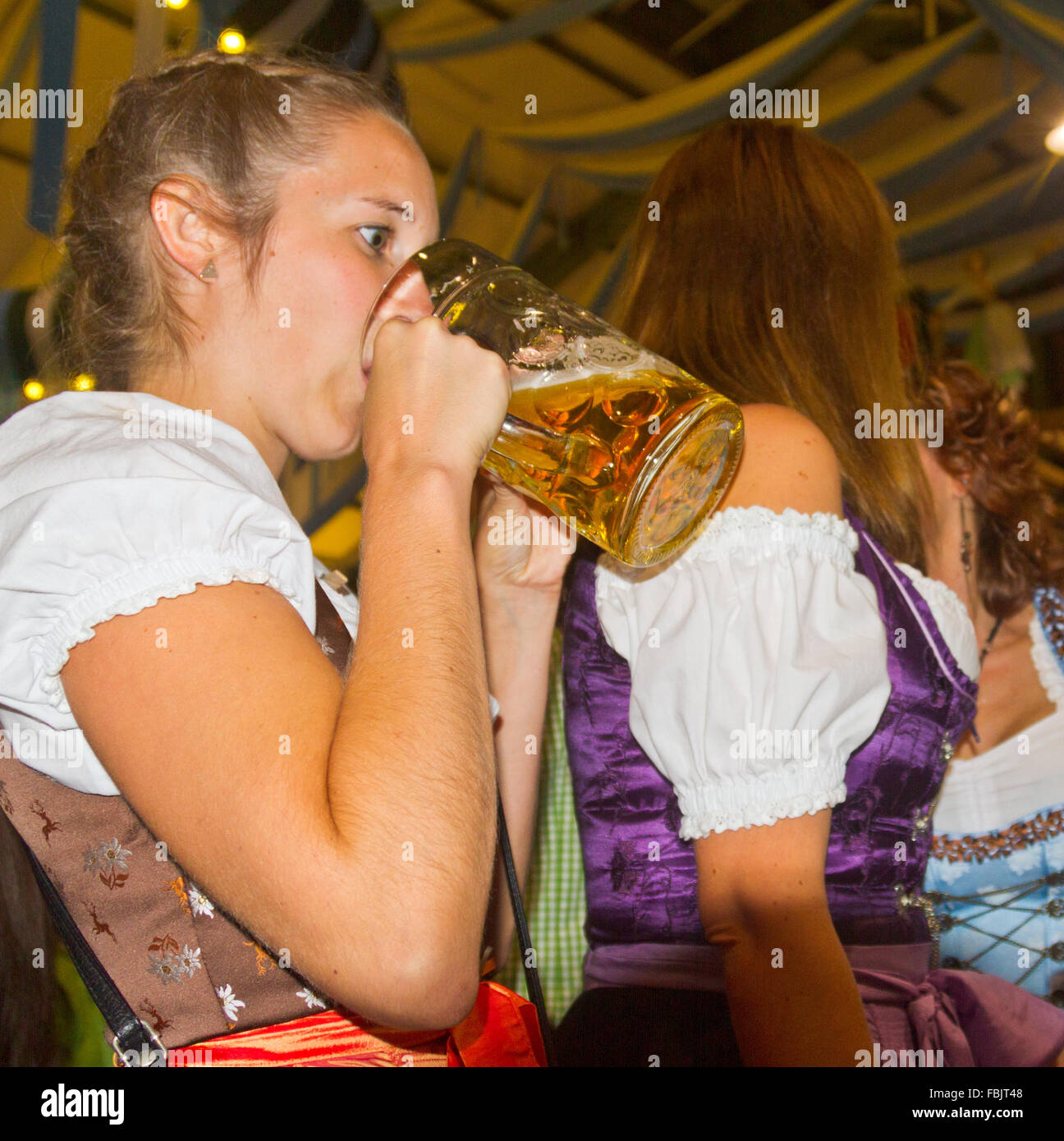 Mit weit aufgerissenen Augen junge Frau trinken Bier aus einem Stein in einem Bierzelt auf dem Oktoberfest in München, Deutschland Stockfoto