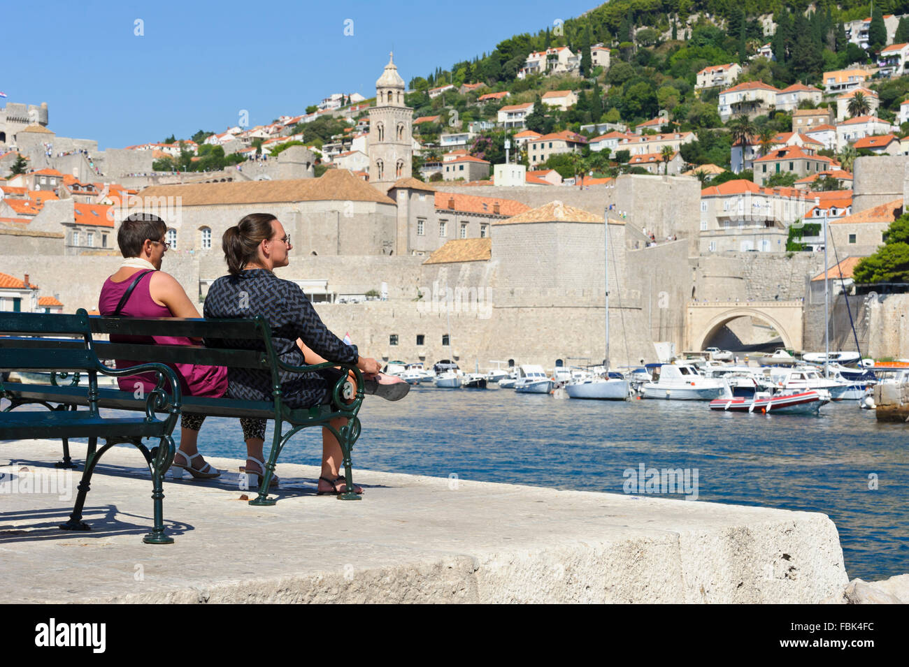 Zwei Frauen sitzen auf einer Bank auf dem Pier am Hafen von Dubrovnik, Kroatien. Stockfoto