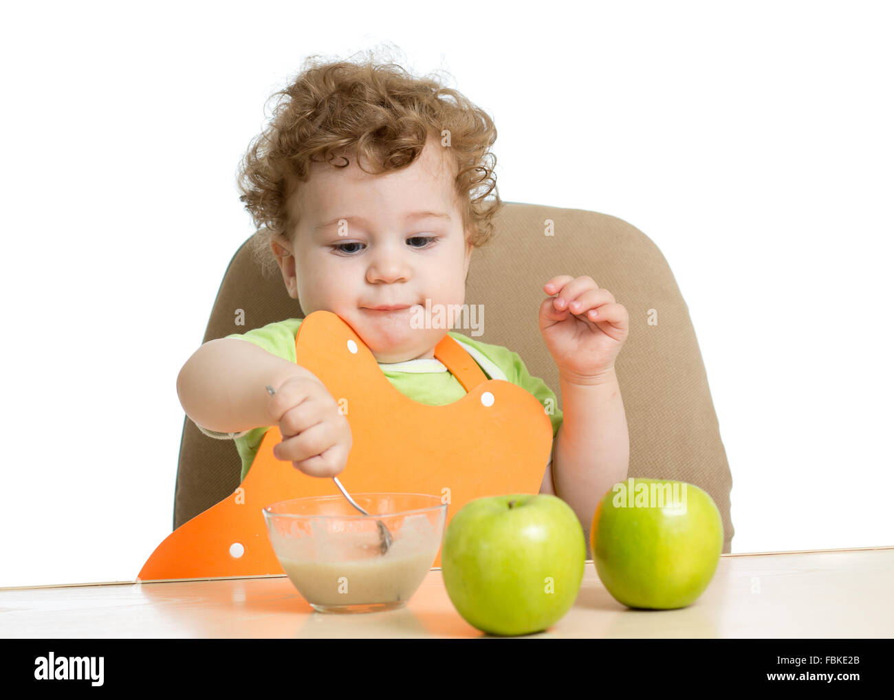 kleines Kind isst mit Löffel sitzen am Tisch mit Früchten Stockfoto
