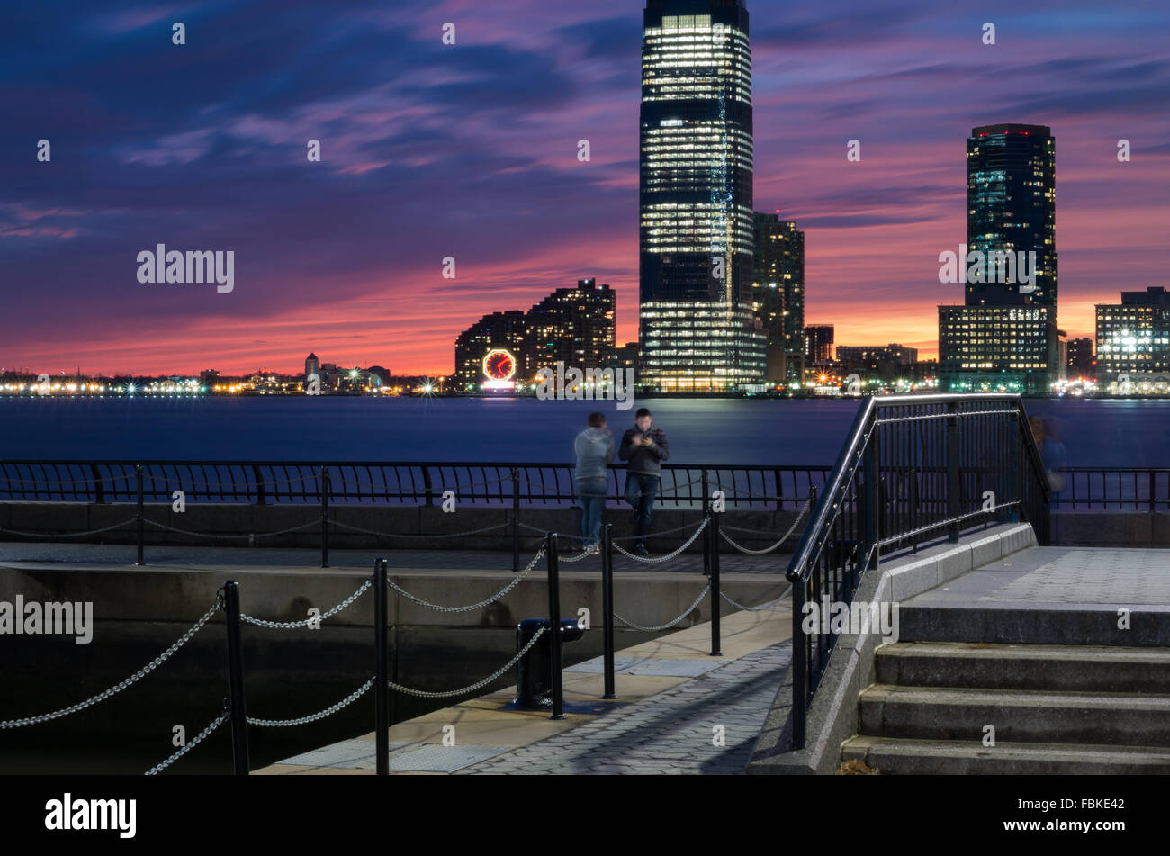 Lange Exposition Blick auf den Sonnenuntergang mit World Financial Plaza und zwei Männer stehen und Jersey City Türme im Hintergrund. Stockfoto