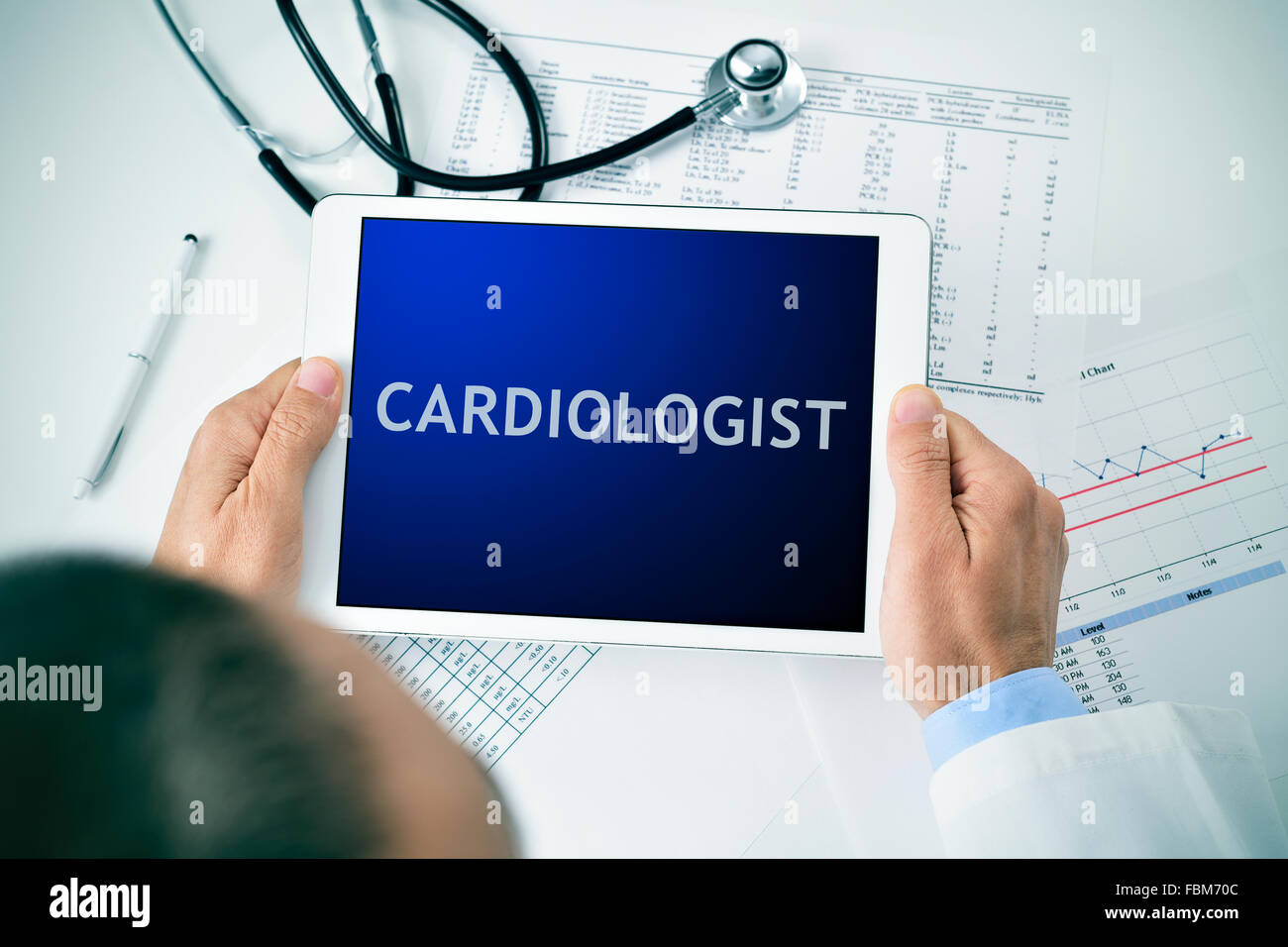 Nahaufnahme von einem Arzt Mann sitzt an seinem Schreibtisch einen Tablet-Computer mit dem Wort Kardiologen in seinem Bildschirm halten Stockfoto