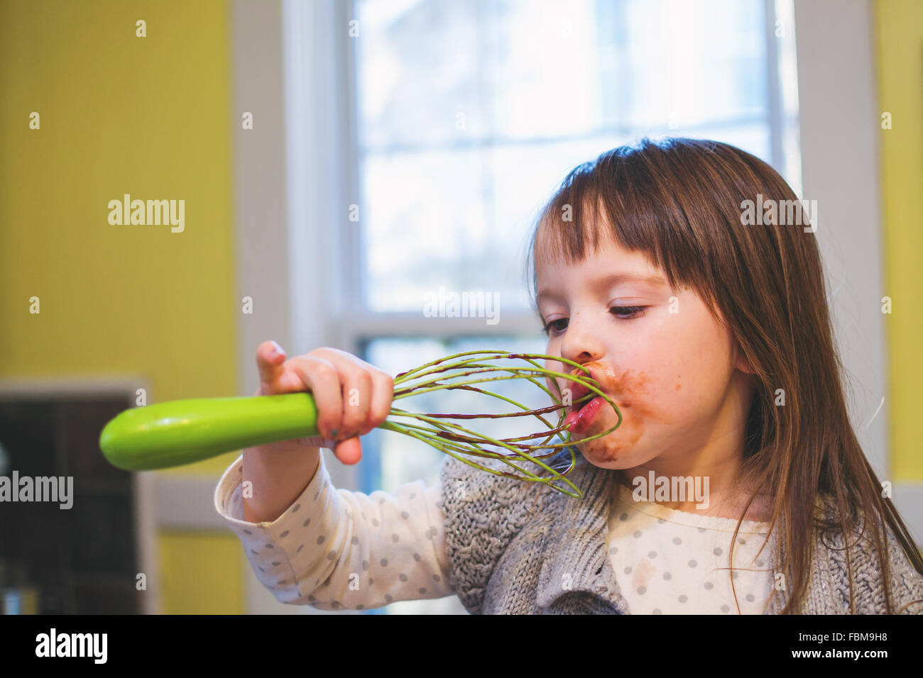 Mädchen lecken Schokolade Kuchen-Mix aus einem Schneebesen Stockfoto