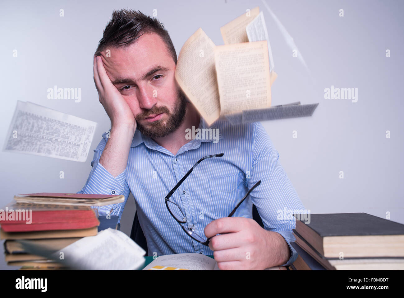 Frustriert Mann ruht der Kopf in der hand mit Büchern und Papieren herumfliegen Stockfoto
