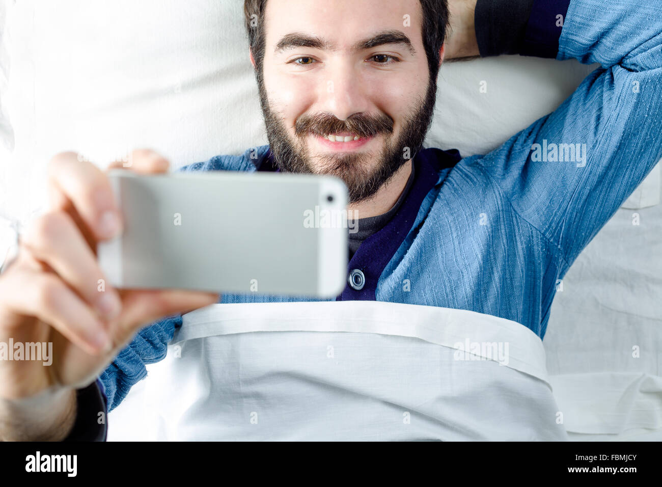 Lächelnder Mann mit Pyjamas, wobei ein Selbstporträt mit einem Smartphone Stockfoto