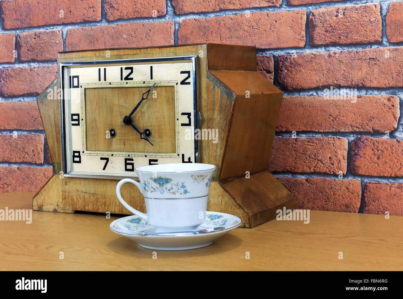Hölzerne Mantel Vintage Art-déco-Uhr mit alten roten Ziegel Wand Effekt Hintergrund und China Teetasse und mit Tee gefüllt Stockfoto