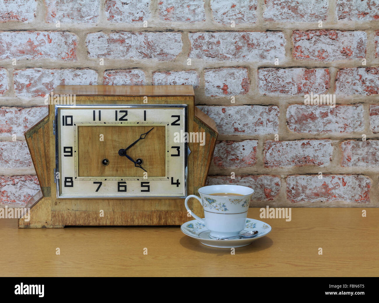 Hölzerne Mantel Vintage Art-déco-Uhr mit alten Ziegel Wand Effekt Hintergrund und China Teetasse und mit Tee gefüllt Stockfoto