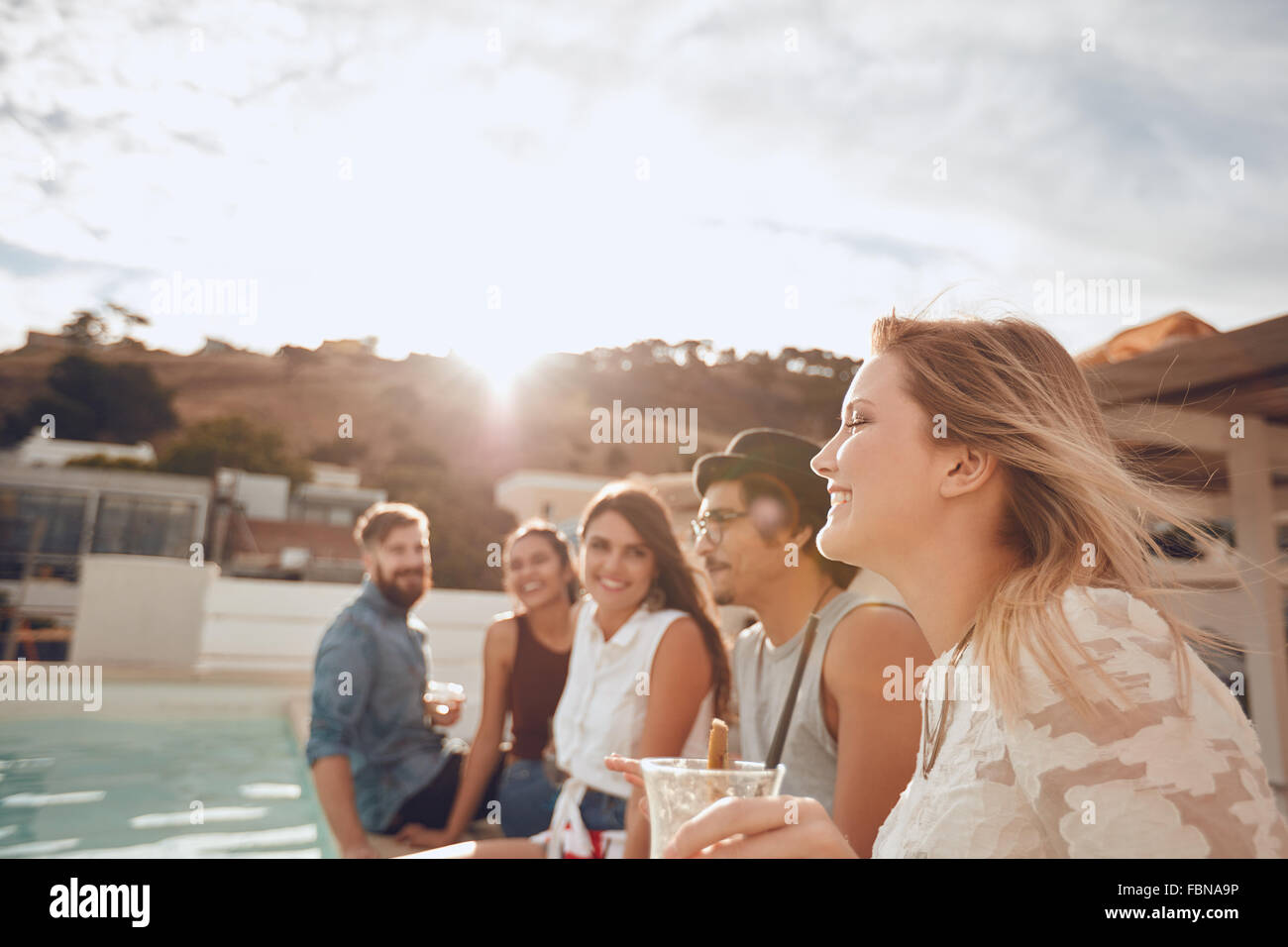 Gruppe von Freunden sitzen in einer Reihe am Rande des Schwimmbad und genießen Partei. Fröhliche junge Menschen mit einer Party auf dem Dach Stockfoto