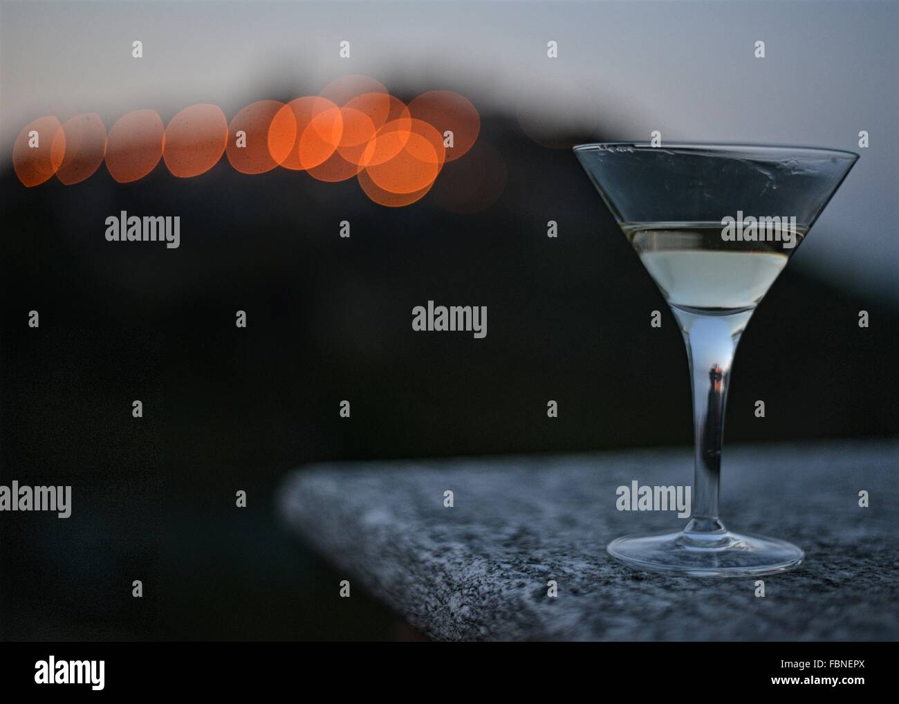 Cocktail Glas auf Granit Oberfläche. im Freien, am späten Abend, Beleuchtung der alten Bergort auf Hintergrund. Barolo, Italien. Stockfoto