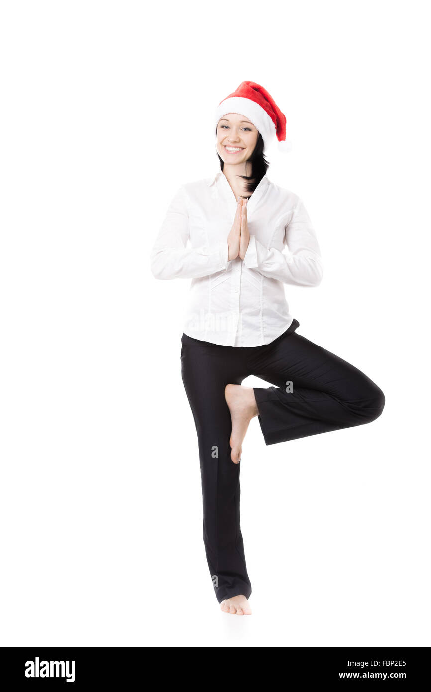 Lächelnd in festlich gekleidet in weißen Hemd und rote Weihnachtsmann Weihnachtsmütze, stehend in Yogaposition weibliche junge Büro Stockfoto