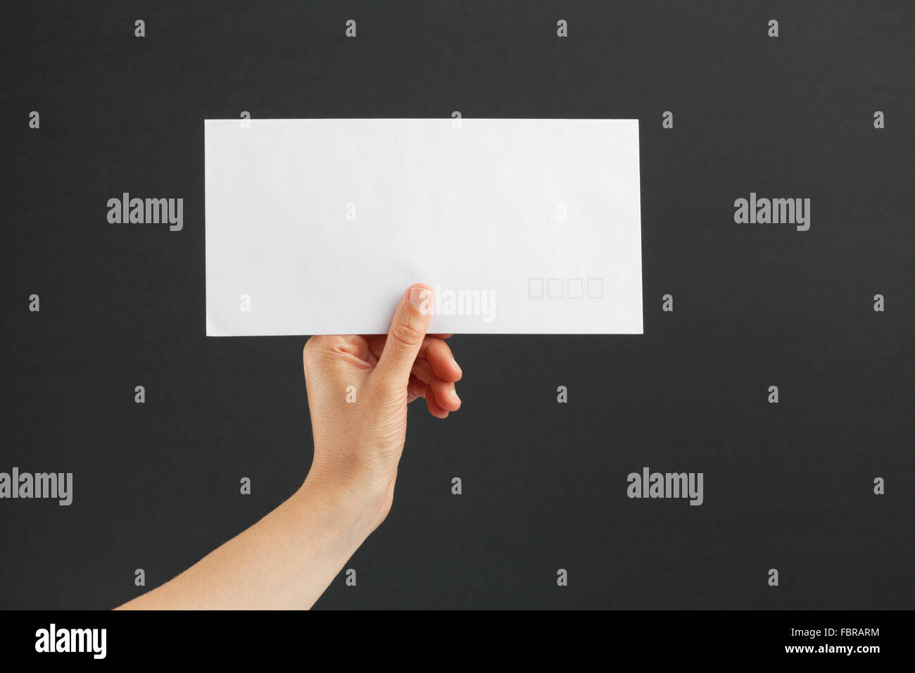 Weibliche Hand, die einen weißen Porto Umschlag auf schwarzem Hintergrund Stockfoto