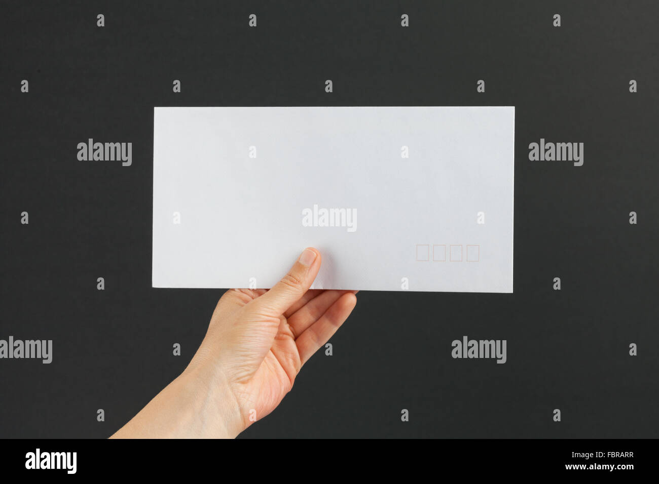Weibliche Hand liefern einen weißen Porto Umschlag auf schwarzem Hintergrund Stockfoto