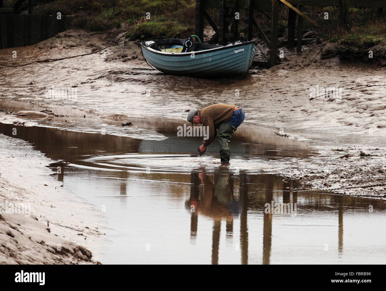 Ein Mann seinen schlammigen waschen die Hände in den Bach am Dornweiler Hafen an der Küste von North Norfolk. Stockfoto