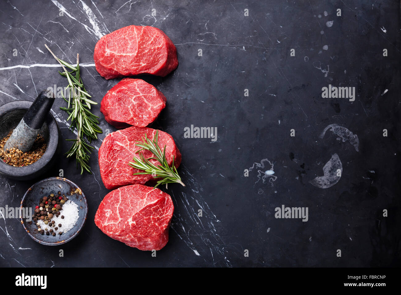 Rohes frisches marmoriertes Fleisch Steak und Gewürze auf dunklem Marmor Stockfoto