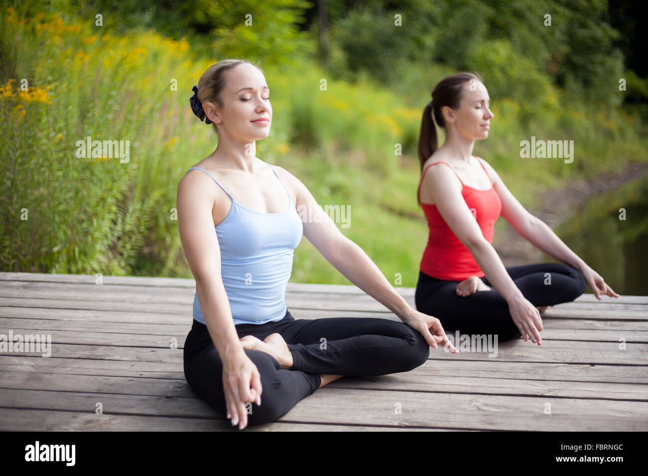 Zwei ruhige junge schöne Frauen auf Meditations-Sitzung im Freien sitzt ...
