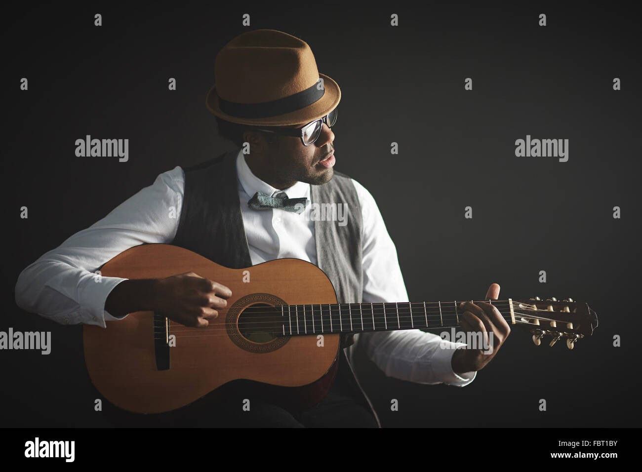 Eleganter junger Mann in intelligente Kleidung und Hut, Gitarre spielen Stockfoto