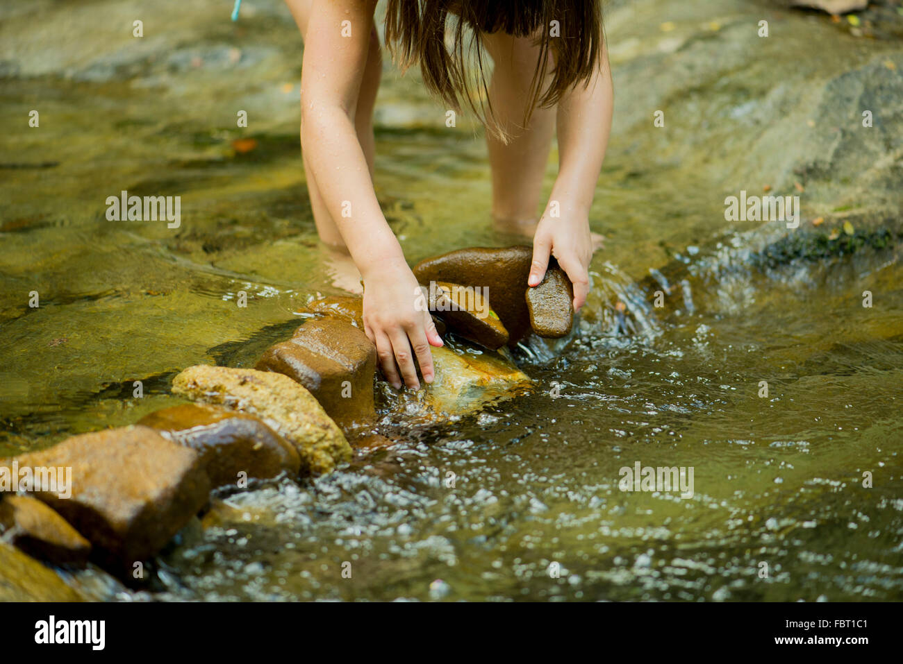Kind mit Felsen zum Bau eines Staudamms in einem seichten Bach Stockfoto
